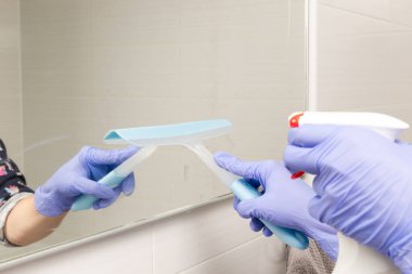 Yakın plan kadın elleri banyo aynasına temizleyici serpiştirir ve siler.