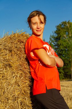 Gün batımında saman yığını ve ormanın arka planında kırmızı tişörtlü güzel bir kızın portresi.