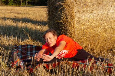 Spor üniformalı genç bir kız gün batımında samanlığın arka planında yoga yapıyor.