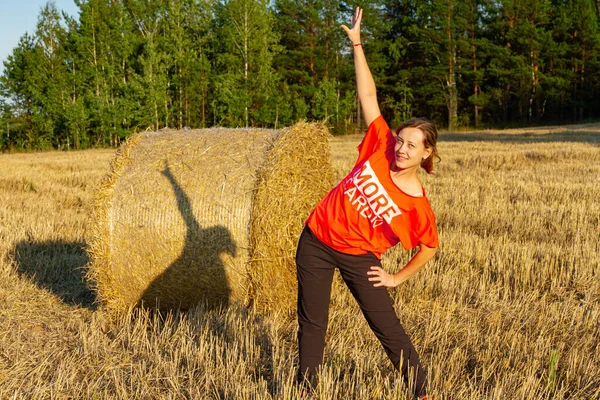 穿着运动服的年轻漂亮的姑娘在草堆边的田里做体操 — 图库照片