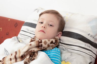 Yatağında eşarbı olan mavi kazaklı hasta çocuk iyileşmeyi bekliyor.