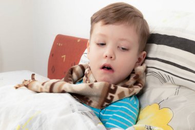 Yatağında eşarbı olan mavi kazaklı hasta çocuk iyileşmeyi bekliyor.