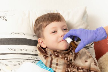 Mavi eldivenli anne hasta bir çocuğun burnuna ilaç serpiyor.