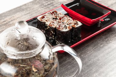 Çaydanlık, bitkisel çaydanlık ve gri granit taşın üzerinde yılan balığı ve susam tohumlu rulo.