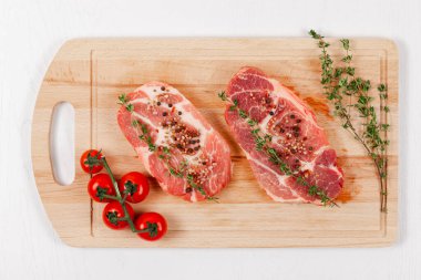 Baharatlı, domatesli ve kekik dilimlenmiş taze domuz bifteği beyaz ahşap bir masada mutfak tahtasında.