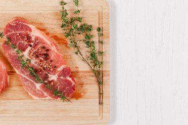 Baharatlı taze domuz bifteği ve kekik beyaz ahşap bir masada mutfak tahtasının üzerinde.