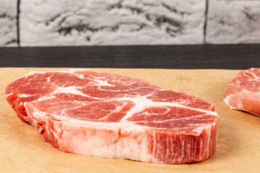 Siyah masadaki kahverengi parşömen kağıdında gri tuğla duvar zeminine karşı taze çiğ et domuz eti.