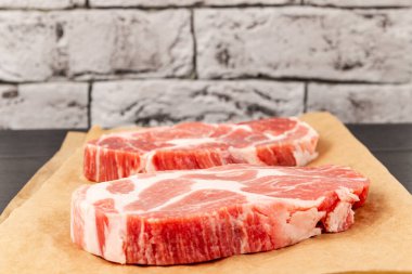 Siyah masadaki kahverengi parşömen kağıdında gri tuğla duvar zeminine karşı taze çiğ et domuz eti.