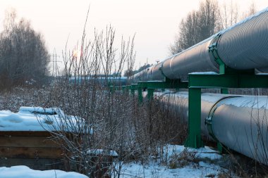 Koruyucu metal bir termal yalıtım ceketinin içindeki merkezi ısıtma boruları soğuk bir kış akşamı gün batımında yerin üstünde yatıyordu.