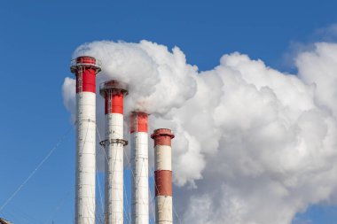 Kazan dairesinin kırmızı-beyaz bacaları, trafik ışığı ile donatılmış. Güneşli kış gününde mavi gökyüzüne karşı beyaz duman.