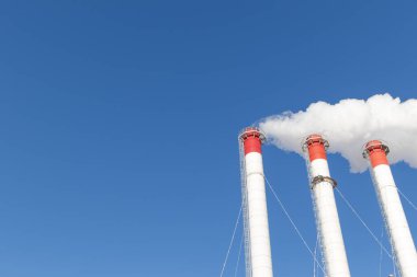 Kazan dairesinin kırmızı-beyaz bacaları, trafik ışığı ile donatılmış. Güneşli kış gününde mavi gökyüzüne karşı beyaz duman.