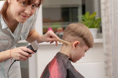 Genç anne kuaför karantina sırasında bebeğini saç makasıyla keser. Seçici odaklanma. portre