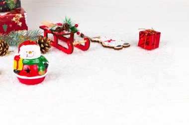 Kardan adam, hediyeli kutular, Noel ağacı konisi ve dalı, Noel Baba kızağı ve beyaz kar arka planında altın çan.