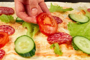 Kadın eli soslu, salatalıklı, salatalıklı ve salamlı taze sebzelerin üzerine doğranmış taze sebzeler koyar. Seçici odaklanma. Kapat.