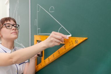 Tahtadaki sınıftaki öğretmen genç bayan cetvelle bir üçgen çiziyor. Portre. Kapat.