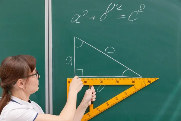 黒板のクラスの若い女教師が定規で三角形を描く 肖像画 閉めて — ストック写真