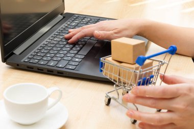 Siyah dizüstü bilgisayarın arka planında kutular ve masanın üstünde kahve fincanı olan metal krom araba. Çerçevede kadın elleri var. seçici odak