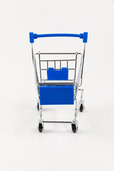 Empty Metal Shiny Grocery Cart Wheels White Wooden Table Background — Stock Photo, Image