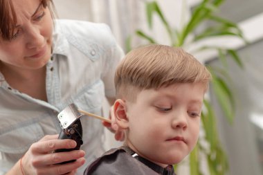 Genç anne kuaför karantina sırasında bebeğini saç makasıyla keser. Seçici odaklanma. portre