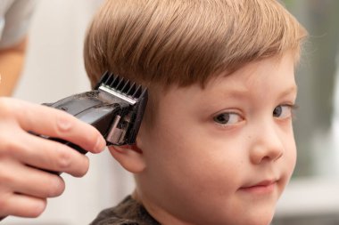 Kadın eli saç makasıyla kesilmiş sevimli bir anaokulu çocuğunun yakın plan portresi. Kameraya bak. seçici odak