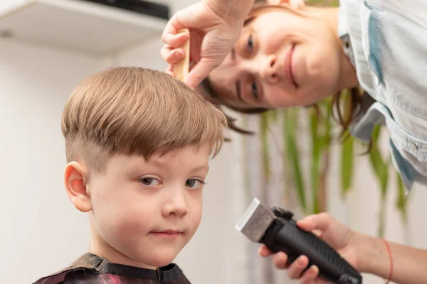 若いママの美容師は隔離中に子供を自宅でヘアクリッパーで切断します 選択的集中 肖像画 — ストック写真