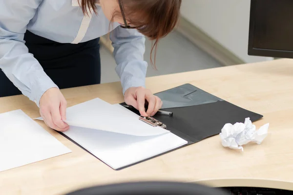 female hands in a blue blouse in the office at a wooden work table looks through documents in a black folder