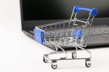 Tekerlekli metal krom market arabası beyaz tahta bir masada siyah bir dizüstü bilgisayarın arka planında. seçici odak