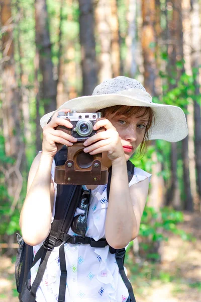 夏日阳光明媚 年轻的女孩戴着草帽 背着背包和照相机在森林里绿树的背景下观光 有选择的重点 — 图库照片