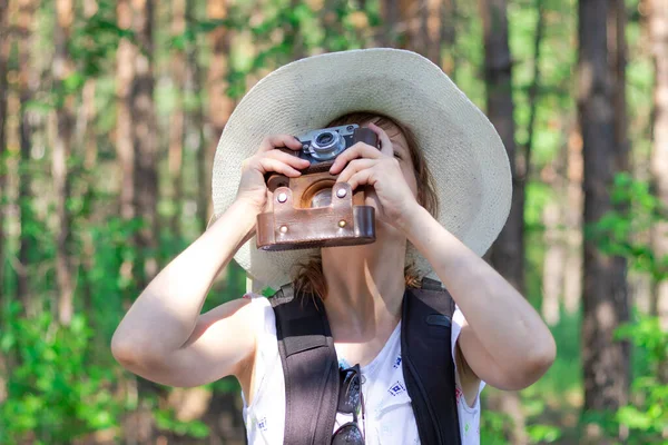 夏日阳光明媚 年轻的女孩戴着草帽 背着背包和照相机在森林里绿树的背景下观光 有选择的重点 — 图库照片
