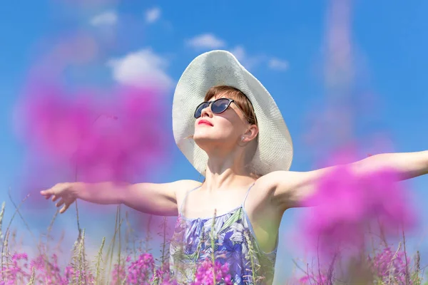 美丽的年轻女子戴着帽子 戴着太阳镜 在一个炎热的夏天 在蓝天的映衬下 在一片鲜花的田野里 有选择的重点 后续行动 — 图库照片