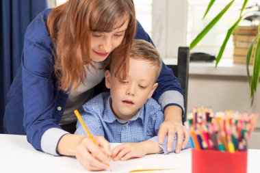 Yedi yaşında tatlı bir çocuk salgın sırasında annesiyle birlikte beyaz tahta bir masada ödev yapıyor. Seçici odaklanma. Yakın plan. Portre