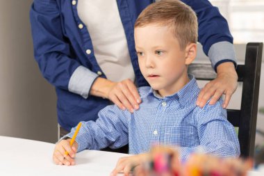 Yedi yaşında tatlı bir çocuk salgın sırasında annesiyle birlikte beyaz tahta bir masada ödev yapıyor. Seçici odaklanma. Yakın plan. Portre