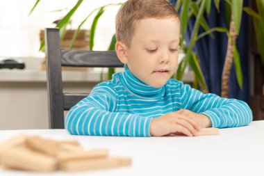 Evinde, beyaz bir tahta masada arka planda ışık penceresinin önünde Jenga oynayan yedi yaşında tatlı bir çocuk. Seçici odaklanma. Yakın plan. Portre