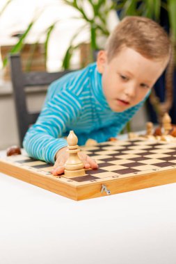 Evde beyaz tahta bir masada satranç oynayan yedi yaşında tatlı bir çocuk. Seçici odaklanma. Yakın plan. Portre