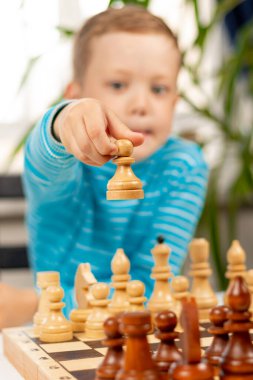 Evde beyaz tahta bir masada satranç oynayan yedi yaşında tatlı bir çocuk. Seçici odaklanma. Yakın plan. Portre
