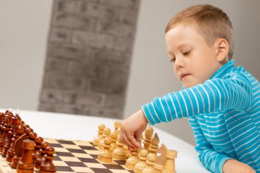 Evde beyaz tahta bir masada satranç oynayan yedi yaşında tatlı bir çocuk. Seçici odaklanma. Yakın plan. Portre