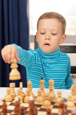 Evde beyaz tahta bir masada satranç oynayan yedi yaşında tatlı bir çocuk. Seçici odaklanma. Yakın plan. Portre