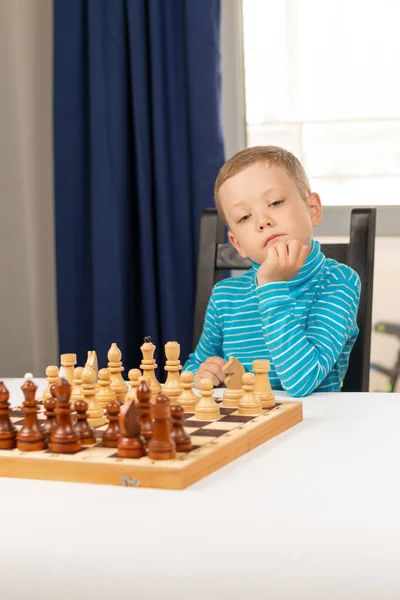 Menino fofo de 5 anos jogando xadrez sozinho em seu quarto em casa