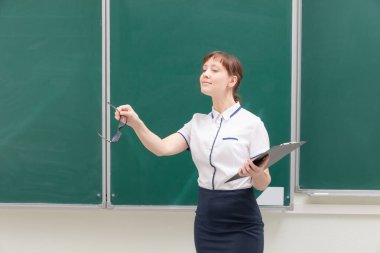 Okul öğretmeni, beyaz bluzlu, elinde klasör ve elinde gözlüklerle tahtada arka planda duran genç ve güzel bir kadın. portre