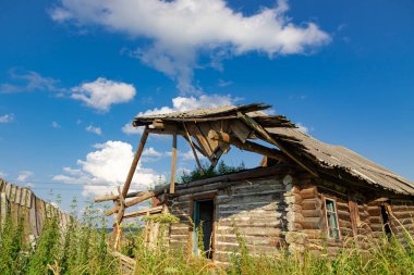 Eski ahşap kırsal, terk edilmiş bir evi beyaz bulutlu mavi bir gökyüzüne karşı güneşli bir yaz gününde harap etti. Yakın plan. Manzara