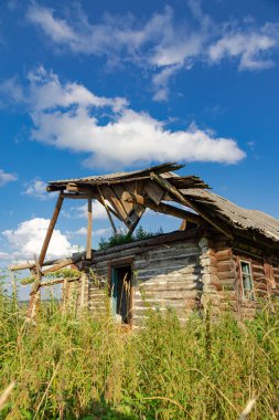 Eski ahşap kırsal, terk edilmiş bir evi beyaz bulutlu mavi bir gökyüzüne karşı güneşli bir yaz gününde harap etti. Yakın plan. Manzara