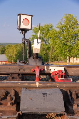 Köydeki tren yolunda trafik ışığı ormanın arka planına ve açık güneşli bir yaz gününde beyaz bulutlu mavi gökyüzüne karşıdır. Yakın plan.