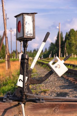 Köydeki tren yolunda trafik ışığı ormanın arka planına ve açık güneşli bir yaz gününde beyaz bulutlu mavi gökyüzüne karşıdır. Yakın plan.