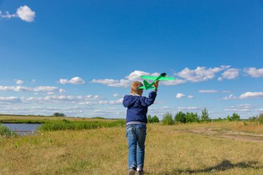 Mavi ceketli altı yaşındaki anaokulu öğrencisi bir yaz günü bulutlu mavi gökyüzüne karşı bir oyuncak uçak fırlatıyor. Parlak güneş parlıyor. Manzara
