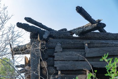 Mavi gökyüzüne karşı aydınlık bir yaz gününde köyde yanmış eski ahşap bir ev. Yakın plan.
