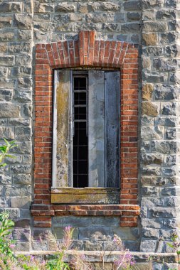 Doğal gri taştan bir duvarın içindeki antik bir kalenin kırmızı tuğladan penceresi. Kemerli inşaat. Yaz güneşli bir gün. Yakın plan.
