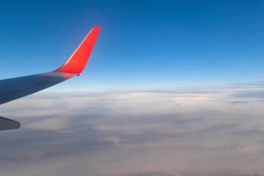 Parlak güneşin altında, uçağın penceresinden, bulutların üzerinden yükselen mavi, berrak gökyüzünün görüntüsü. Çerçevedeki bir uçak kanadının parçası