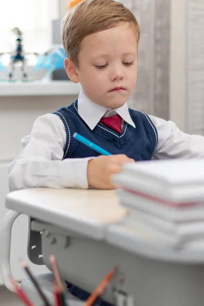 学校の制服を着た可愛い少年1年生が自宅で鉛筆を手に机に座りながら宿題をする 遠隔教育 選択的フォーカス 接近中だ 肖像画 — ストック写真