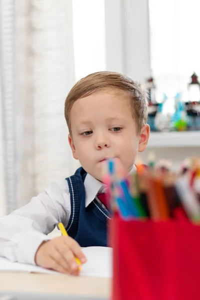 学校の制服を着た可愛い少年1年生が自宅で鉛筆を手に机に座りながら宿題をする 遠隔教育 選択的フォーカス 接近中だ 肖像画 — ストック写真