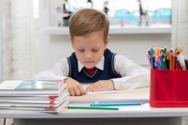 Birinci sınıfa giden, okul üniformalı tatlı bir çocuk teneffüste masasında karton uçak yapıyor. Seçici odaklanma. Portre